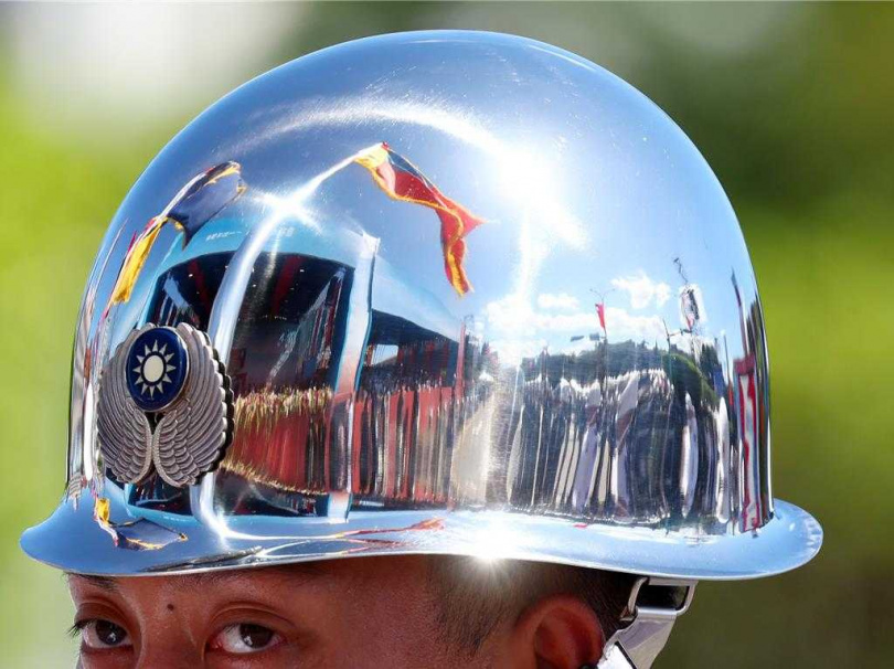 中華民國114年國慶大典10日登場，國防部聯合樂隊在炎熱的天氣中精湛演出《樂儀齊鳴震八方 戮力同心護家邦》。儀隊士兵頭盔反射出總統府前的典禮場景與飄揚的國旗。鏡面般的光影中，藍天與紅旗交錯，象徵國家榮耀與守護的信念。（圖／中國時報鄧博仁攝）