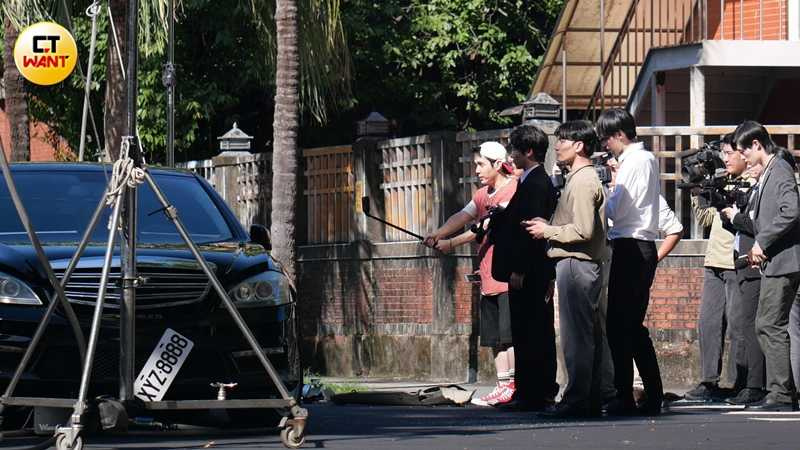 陳彥嘉身穿桃紅色毛線衣反戴一頂白色帽子，造型頗具青春氣息，手持運動相機，與一群像是扮演攝影記者的臨演拍攝撞車現場。（圖／本刊攝影組）