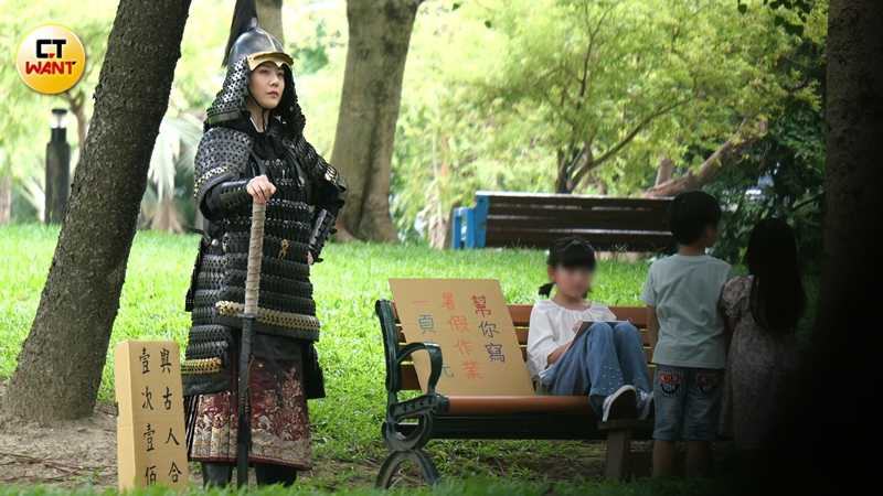 武將裝扮的韓瑜手握長刀喊著「與古人合照一次一百」，而坐在椅子上的小女孩身邊紙牌寫著「幫你寫暑假作業一頁十元」，畫面相當好笑。（圖／本刊攝影組）