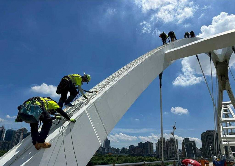 新月橋屬於特殊輕型橋梁，橋面載重有限，無法使用大型高空作業車維修，必須依賴工業繩索技術員以懸吊方式進場作業。（圖／新北市高灘處提供）