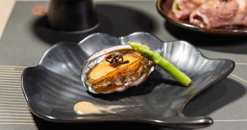 台北旭集三間門市推出期間限定料理〈嫩煎鮑魚佐蕈菇奶油醬〉，主廚先將飽滿厚實的鮑魚煎至表層些微酥香，點綴蕈菇奶油白醬，再佐以昆布鹽及新鮮蘆筍，甘甜鹹鮮交織。（圖片提供／饗賓集團）