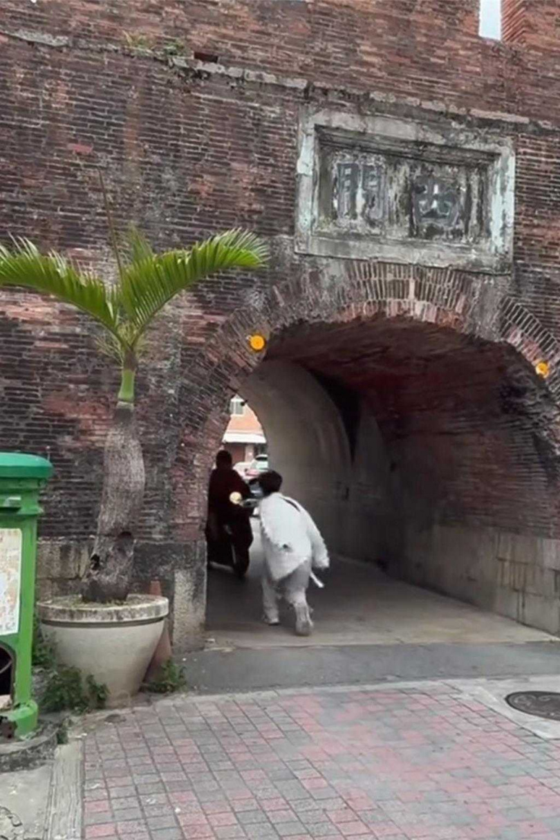 白衣男攀爬恆春西門,最後一躍而下,彈跳起來一轉身,差點與迎面而來的機車碰撞,還好機車及時煞住。(圖/翻攝臉書「恆春半島公共事務討論社團」)