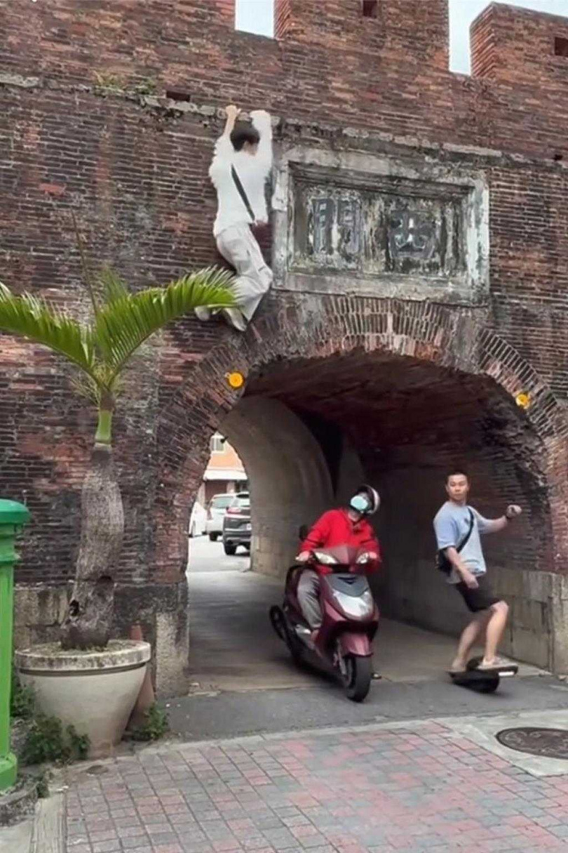 白衣男吊掛在城牆外,底下經過的機車騎士抬頭望著白衣男。(圖/翻攝臉書「恆春半島公共事務討論社團」)