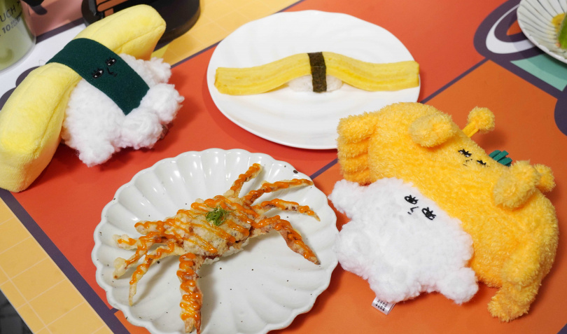 經典人氣品項「軟殼蟹天婦羅壽司」（前，90元）、「翹翹板玉子燒壽司」（40元）同樣有玩偶版，其中軟殼蟹玩偶頭上還可見蔥絲、藏有細節。（圖／魏妤靜攝）