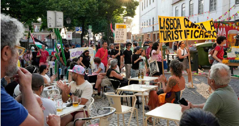 葡萄牙里斯本示威者舉橫幅抗議大眾旅遊，和一旁的遊客形成對比。（圖／達志／美聯社）