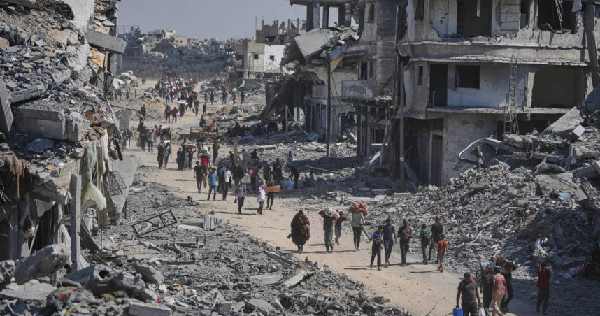 流離失所的巴勒斯坦人帶著他們的物品走過被毀的建築物，返回位於加薩走廊南部汗尤尼斯的家園。（圖／達志／美聯社）