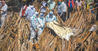 印度首都新德里一處臨時搭建的露天火葬場，一名新冠肺炎病歿者的家屬將其遺體放在木柴上，隨後點火焚燒。由於死亡人數激增，燃燒的木柴不夠，當局開始砍伐市區各處公園的樹木應急。（圖／美聯社）