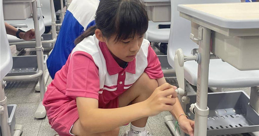 台中市政府自2024年啟動汰換老舊課桌椅計畫，學生示範如何利用搖桿進行課桌椅調整。（圖／台中市府提供）