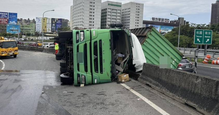 國1桃園交流道有大貨車擦撞護欄翻覆，導致貨櫃掉落倒在車道，造成駕駛手腳擦挫傷。（圖／翻攝畫面）
