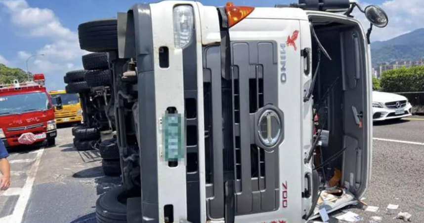 18日下午有1輛貨櫃車行經到國道1號五堵交流道時，整輛車突然側翻在車道上，導致嚴重回堵。消防人員獲報前往救援時，發現貨車已踢破前擋風玻璃脫困，全身僅輕傷。（圖／翻攝畫面）