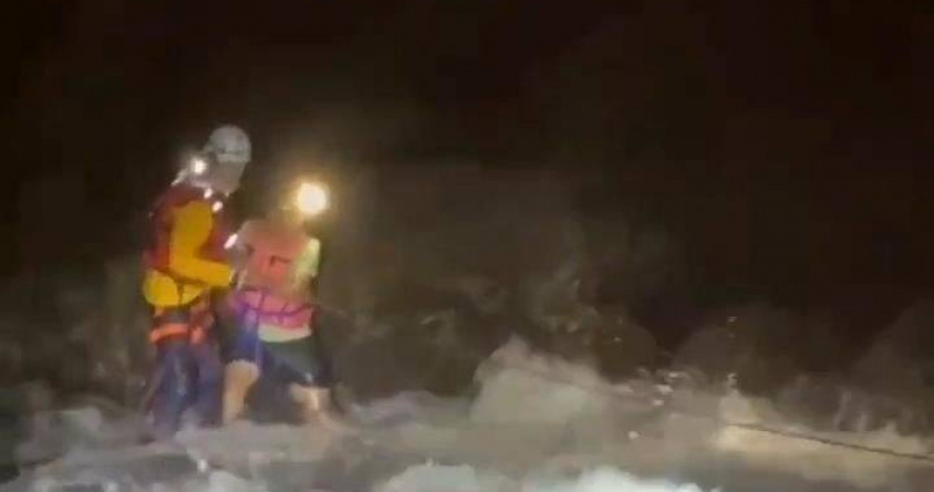 消防人員在貓鼻頭公園海邊架設繩索，於天色昏暗中涉水救援受困釣客。（圖／翻攝畫面）