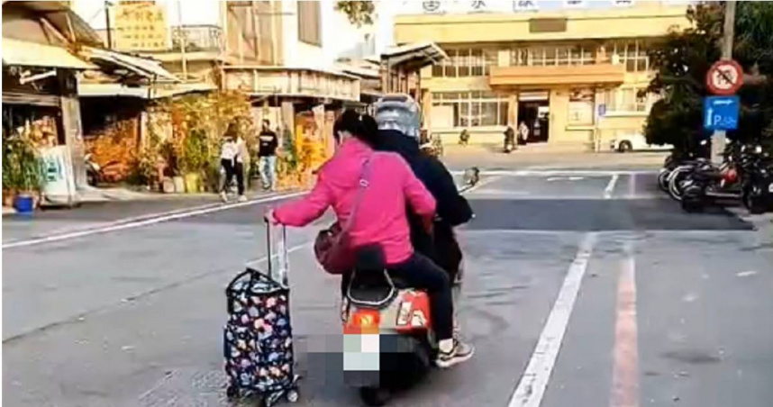 台南市1輛雙載機車後座女子未戴安全帽，竟還手拉著1個附輪購物袋在馬路上滑行。（圖／翻攝畫面）