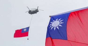 CH-47SD契努克運輸直升機吊掛巨幅國旗，在黑鷹直升機的護衛下通過總統府前的國慶舞台。（圖／黃耀徵攝）