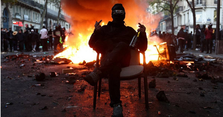 法國當地時間17日爆發大規模反政府示威遊行，一名戴著面具的抗議者坐在燃燒的路障前，封鎖了街道。（圖／達志／路透社）